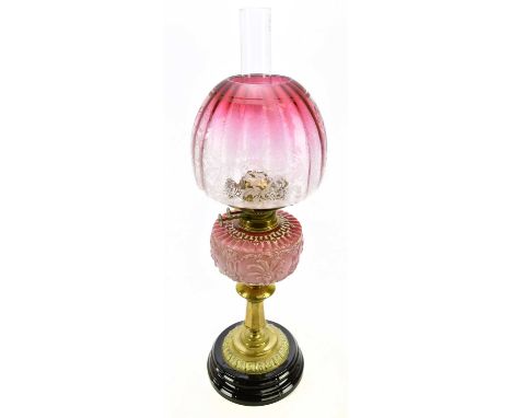 A late Victorian brass oil lamp with dome shaped cranberry and clear glass shade with etched floral decoration above the moul
