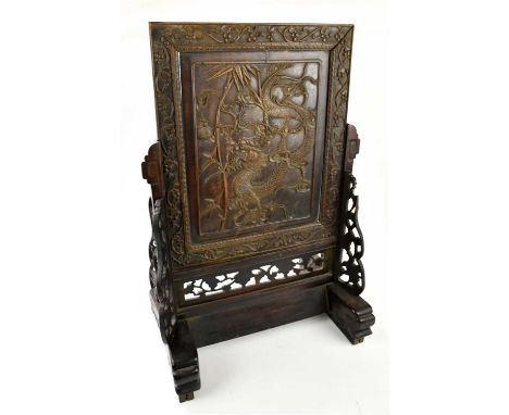 A 19th century Chinese carved hardwood table screen, the panel decorated with a dragon within a fruit and grape vine border, 