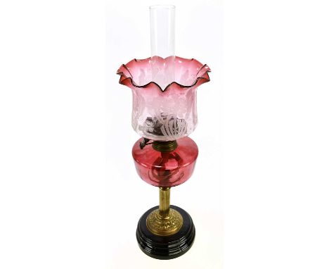 A late Victorian brass oil lamp, with cranberry and clear glass shade with etched floral decoration above the cranberry glass