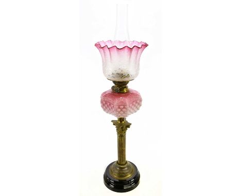 A Victorian oil lamp, with cranberry and clear frosted glass shade, decorated wtih sunflowers above the cranberry and milk gl