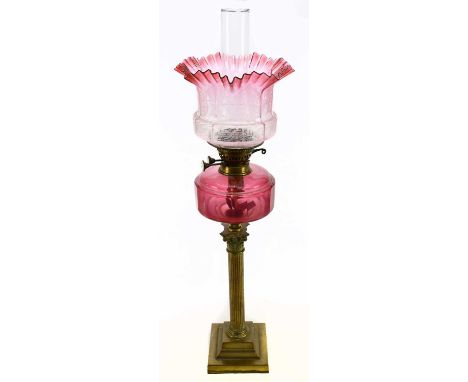 A late Victorian brass oil lamp with cranberry and clear glass shade, with wavy rim, etched with scrolling and floral detail 