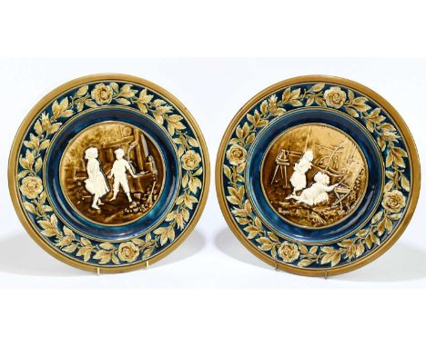 A pair of Austrian ceramic wall chargers, relief decorated with children to the centre inside roses and flowers, diameter 31c
