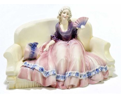KATZHUTTE; a ceramic figure of a maiden with a fan and bonnet seated upon a sofa, impressed and printed marks, length 28cm.Co