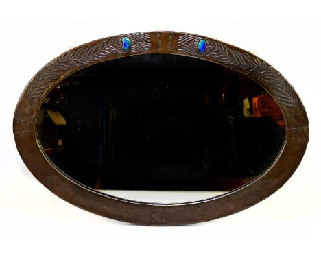 An Arts and Crafts sheet copper and enamel wall mirror of oval form, relief decorated with peacock feathers, 46 x 68cm.Condit