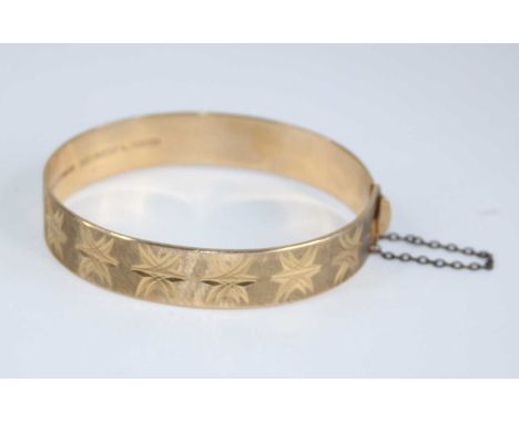 A 9ct gold hinged bangle, having bright cut engraved decoration, with gilt metal safety chain, sponsor NYMPH, 23.5g, dia.6cm,