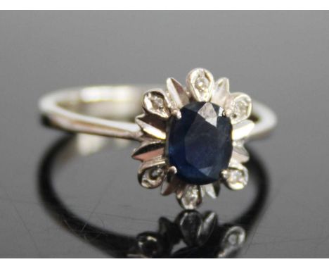 A white metal, sapphire and diamond flower head cluster ring, arranged as a four-claw set oval cut sapphire within a surround