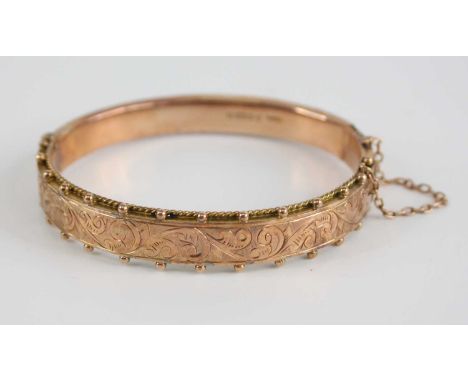 An Edwardian 9ct gold hinged hollow bangle, one side having engraved scroll leaf decoration within a beaded border, with safe