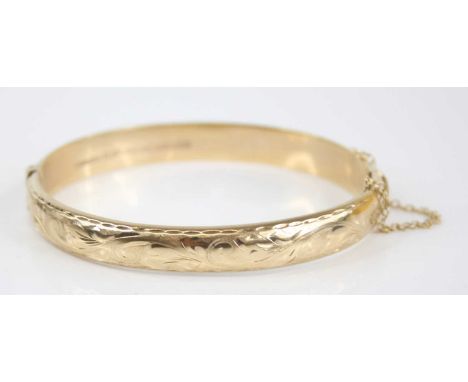 A Victorian style 9ct gold hinged bangle, having stipple engraved and carved leaf decoration, hinge action with safety chain,