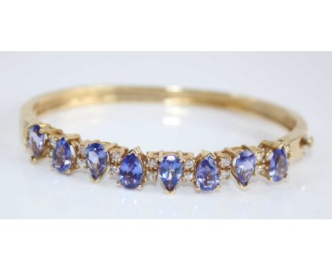 A contemporary yellow metal, tanzanite and diamond set hinged bangle, arranged as eight pear cut tanzanite, each measuring ap