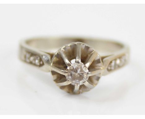 A white metal diamond solitaire ring, the claw set round cut measuring approx 0.12 carats, the shoulders each set with twin d