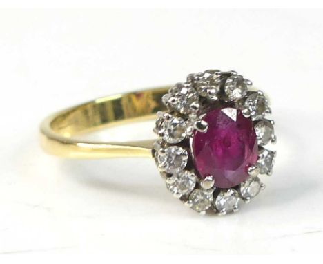 An 18ct yellow and white gold, ruby and diamond oval cluster ring, featuring a centre ruby within a border of 12 round brilli