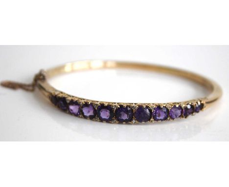 A yellow metal, amethyst and diamond point set hinged bangle, arranged as eleven graduated round cut amethysts, the largest s