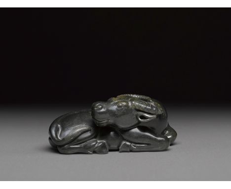 A black jade recumbent water buffaloShown recumbent with its head turned backward, the tail accented with incised parallel li