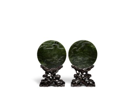 A pair of circular spinach jade plaquesThe disks minimally carved in raised relief to depict tufts of clouds, a stalk of ling