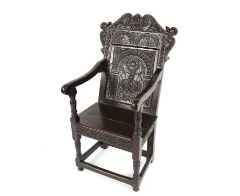 An 18th Century carved oak Wainscot chair having foliate decorated back panel above scroll arms and solid seat, raised on tur