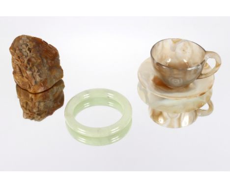 An antique Chinese soapstone boulder carving; a pale celadon hardstone bangle and a finely worked agate cup and saucer (crack