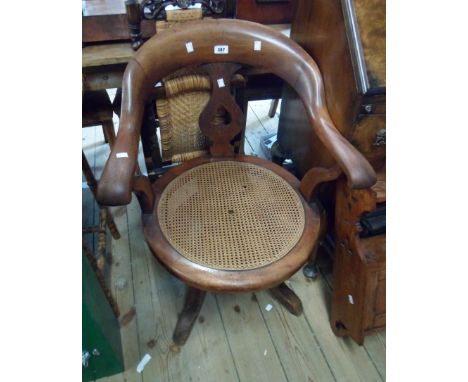 An old mahogany framed bow back swivel elbow chair with damaged rattan seat panel, set on quadrule legs