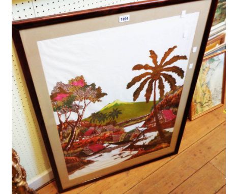 A large format framed batik style print on textile, depicting a tropical scene with waterside buildings and vessels with moun