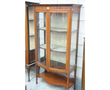 An Edwardian inlaid mahogany bow front display cabinet with 2 glazed doors above a shaped under shelf raised on tapering legs