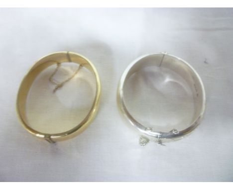 A silver oval bangle with engraved decoration and one other gold plated bangle (2) 