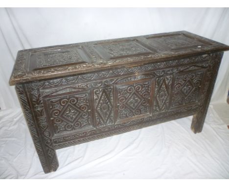 An 18th Century carved oak rectangular coffer with triple panel front, the hinged lid with carved armorial crests on block fe