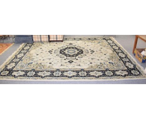 A machine made carpet of Kashan design, the ivory field centred by an indigo medallion, framed by cartouche borders, 400cm by