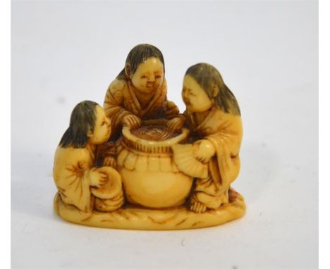 A Japanese ivory netsuke, carved as three Shojo, or other characters, standing beside a large sake jar in a parody of the Thr