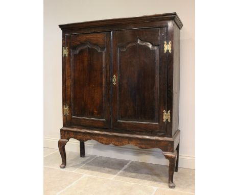 A mid 18th century and later oak cabinet on stand, the moulded cornice above two fielded panel doors and a shaped apron, rais