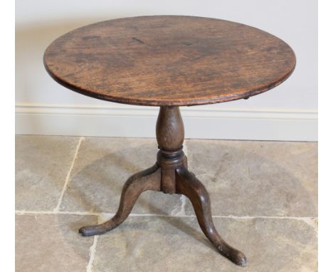 A George III oak tripod table, the circular top raised upon a baluster column extending to three down swept supports and pad 