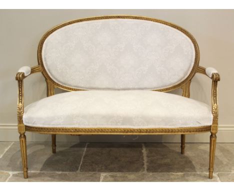 A Louis XVI style giltwood settee, early 20th century, in classical white foliate pattern fabric, the oval padded back within