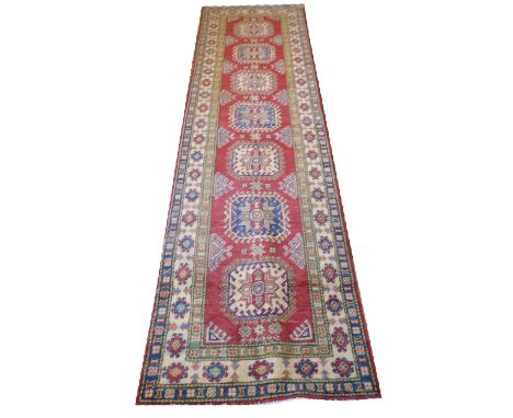 KAZAK RUNNER, 322cm x 83cm, of multiple medallions on ruby field within ivory borders.