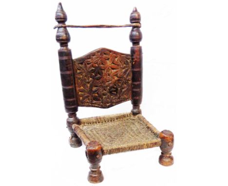 An old Afghan stained cedar wood low tribal chair with sinew strop, carved flower and foliage decoration, woven seat panel an