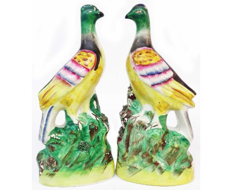 A pair of Staffordshire pottery figurines depicting birds perched on a grassy mound with colourful overglaze enamel painting 