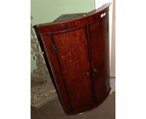 A George III oak and mahogany crossbanded bow fronted hanging corner cupboard