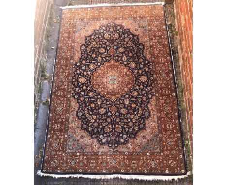 A hand-knotted Caucasian carpet with central red medallion to a dark blue ground profusely decorated with flowers, a red flor