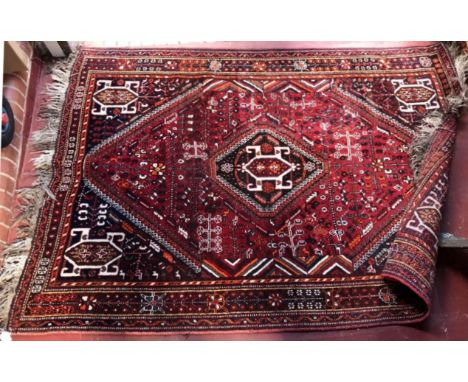 A hand-tufted Caucasian carpet with central medallion to a deep red ground decorated with stylised flowers and a geometric bo