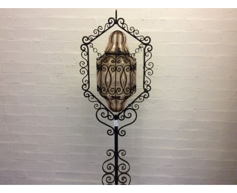A wrought iron scroll design standard lamp with pink bulging glass shade.
