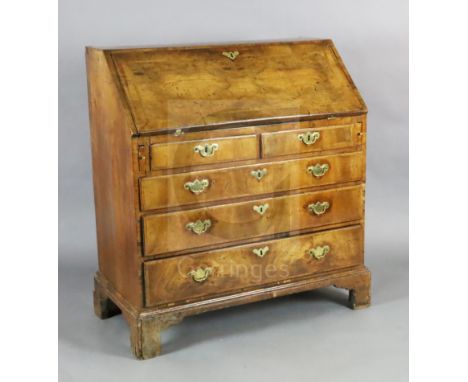 A George II walnut bureau, the fall enclosing pigeon holes and short drawers over two short and three graduated long drawers,