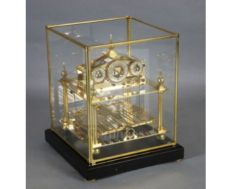 A late 20th century lacquered brass Congreve rolling ball clock, with glazed box and three enamel dials, on an ebonised plint