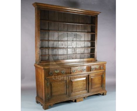 A mid 18th century oak dresser, with boarded three shelf rack, three long drawers and two panelled doors on shaped bracket fe