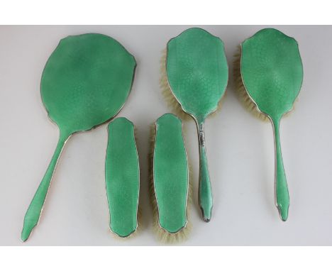A George V silver and green enamel backed dressing table set comprising hand mirror, two hair brushes and two clothes brushes