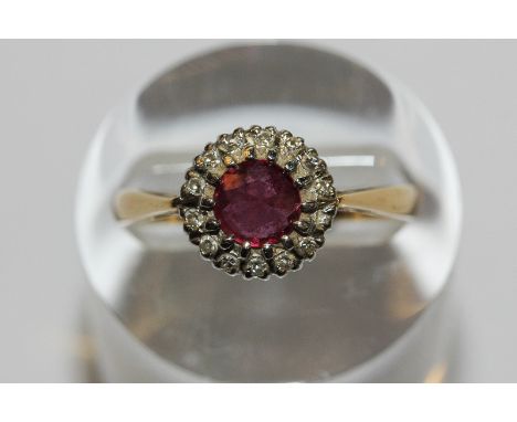 A ruby and diamond ring the circular cut stone multi claw set within a border of small eight cut diamonds in 18ct white and y