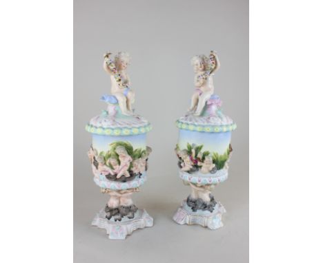 A pair of Sitzendorf porcelain urns and covers, the finial modelled as a cherub holding a garland, the body modelled as water