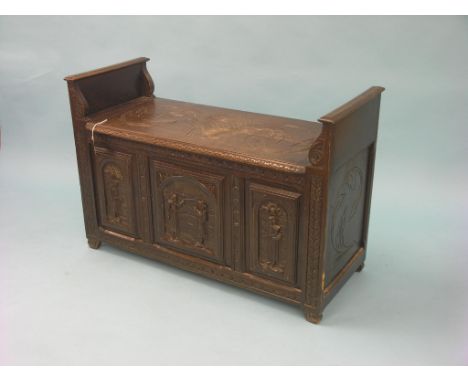 An early 20th century dark oak hall bench, hinged top enclosing storage trunk, the whole carved with figures and foliage in D