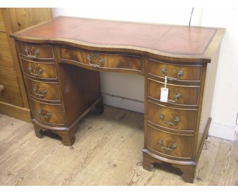 A reproduction mahogany desk, serpentine-fronted with inset leather top, kneehole arrangement of nine drawers, bracket feet, 