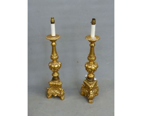 A PAIR OF GILT COMPOSITION BAROQUE STYLE CANDLESTICK LAMPS, THE BALUSTER COLUMNS ABOVE FRUIT KNOPS AND TRIPOD FEET. H 76cms.
