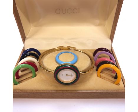 A GUCCI 1100-L GOLD PLATED LADIES BANGLE WATCH WITH TWELVE INTERCHANGEABLE BEZELS, COMPLETE WITH ORIGINAL BOX.  