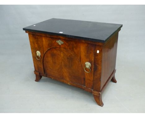 A BLACK MARBLE TOPPED MAHOGANY SIDE CABINET, THE COMPARTMENT DOOR WITH BRASS LION MASK AND RING HANDLES ABOVE SPLAY FEET.   W