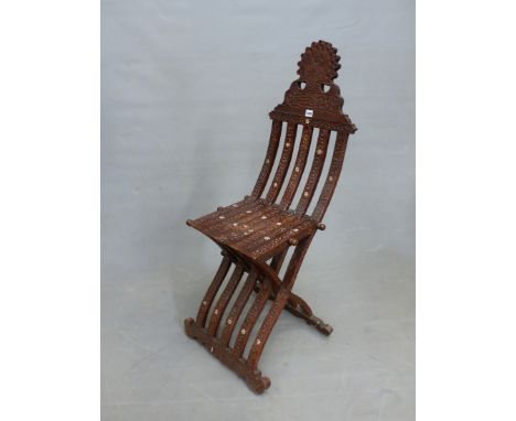 AN ISLAMIC INTAGLIO CARVED HARDWOOD FOLDING CHAIR, THE BARS OF THE BACK AND FRONT LEG INTERLOCKING TO FORM THE SEAT CARVED WI