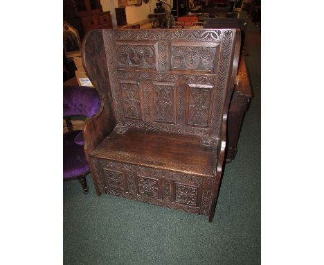 Early 20th century dark oak settle with hinged seat, carved knot and stylized foliage to front and back panel (height 120cm w